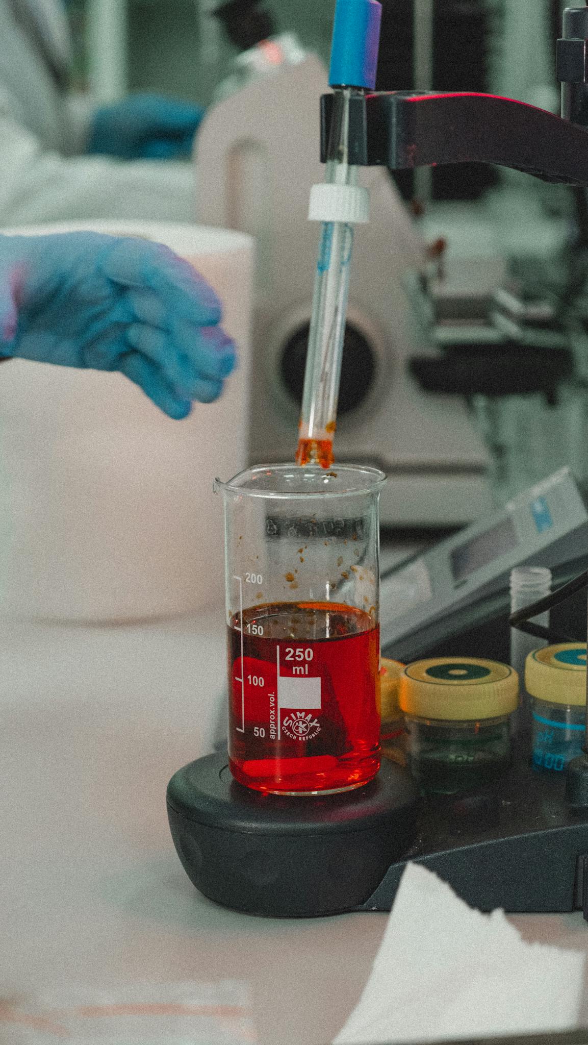 Gloved hands conduct an experiment with red liquid in a laboratory beaker.
